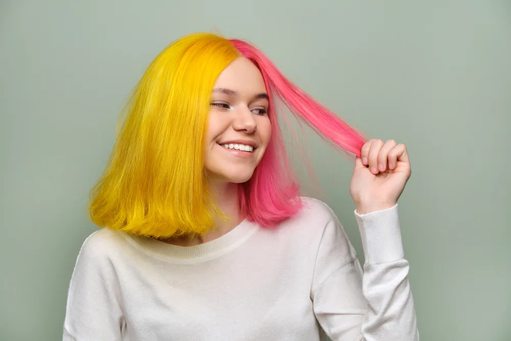 Goldenrod Yellow and Pink Split Dye, one of the best unnatural hair colors for blue eyes, on a woman in a white sweater