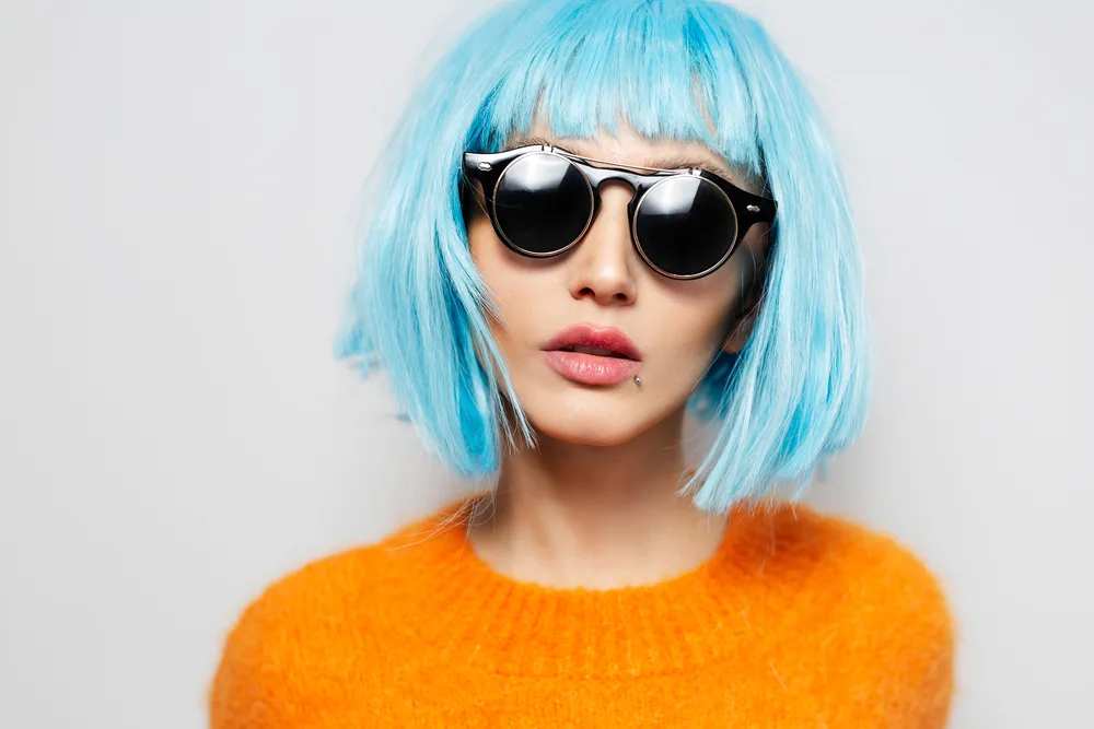 Ice blue, a top pick for unnatural hair colors for blue eyes, on a woman in an orange sweater in a grey room