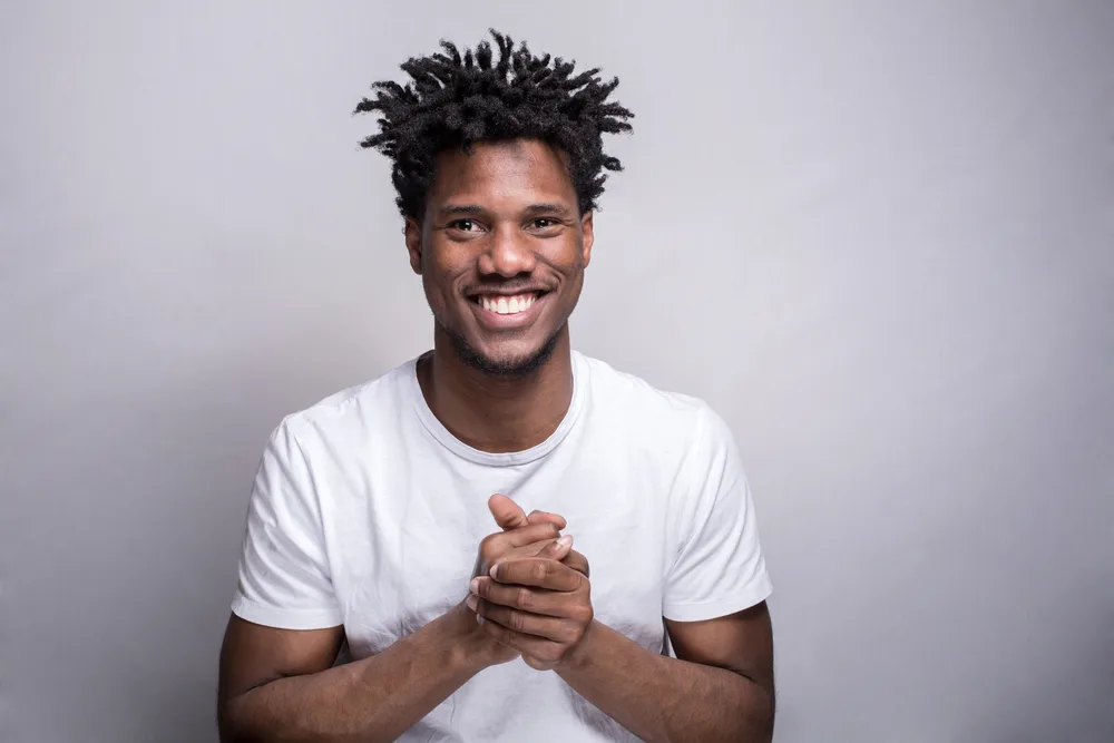 Black man with curly hair cups his hands and smiles for a piece titled will sponging hair damage it