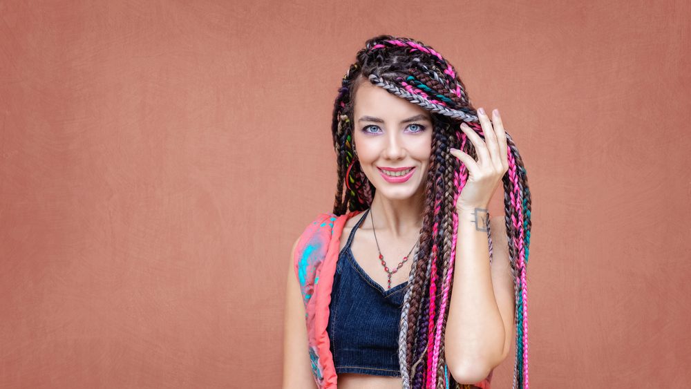 Rainbow drip Thai braids on a woman in a crop top who looks like a hippie