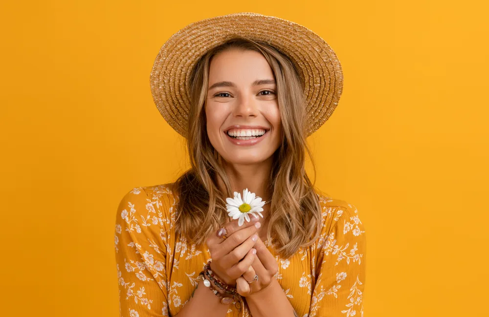 Golden Bronde summer hair color on a woman in a hat in an orange room