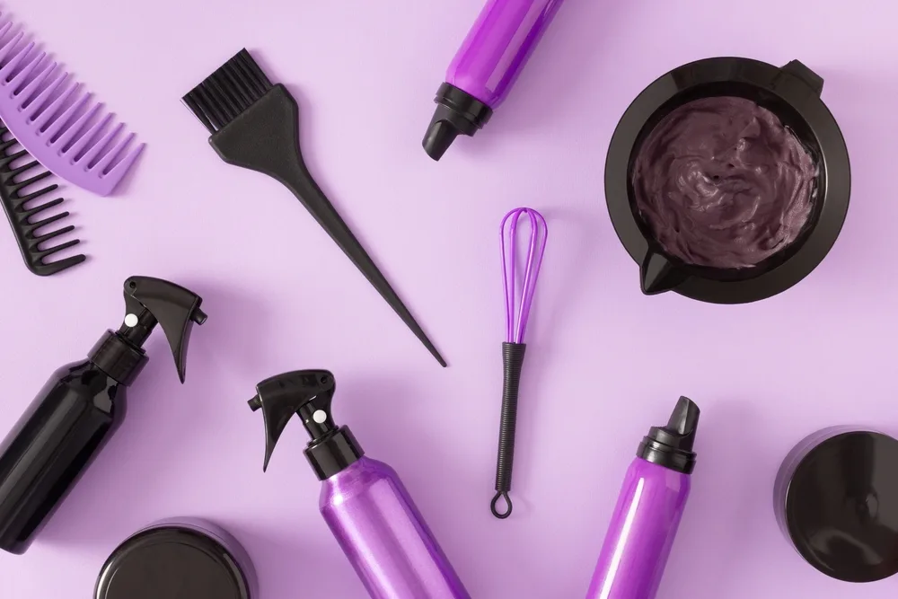 Bowl of the best black hair dye with tools and bottles around it on a purple table