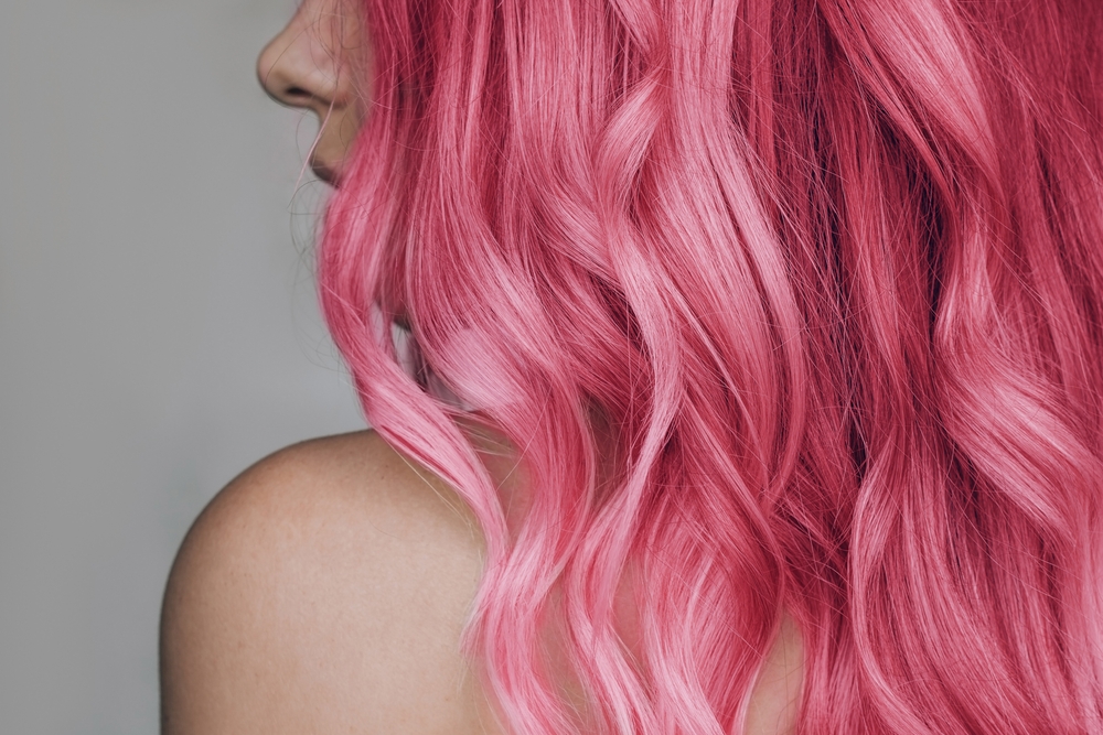 For a guide to the least natural hair colors for cool skin tones, a woman with pink hair looks left