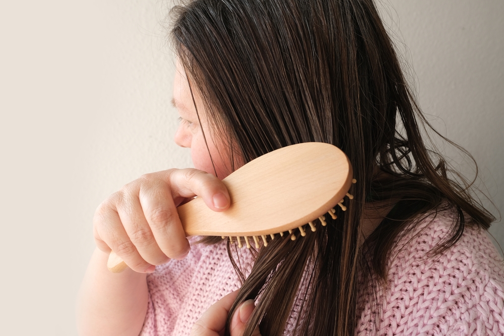 Woman with waxy hair running a wooden brush through the strands