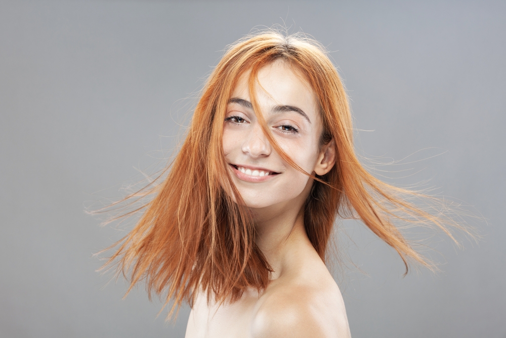 Woman with orange hair smiles for a piece on the best hair colors for blue eyes