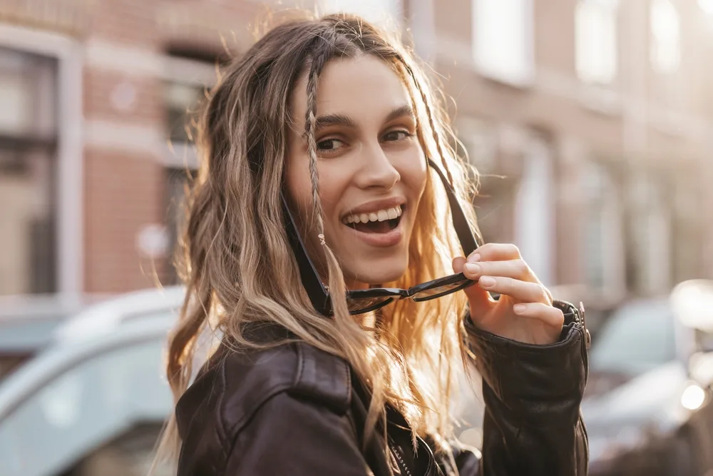 Baby Braids, a throwback y2k hairstyle, pictured on a pensive woman in a leather jacket