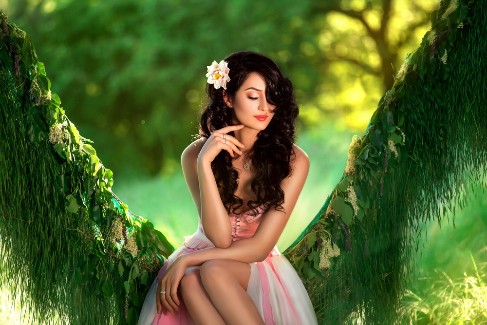 Người phụ nữ có mái tóc đen và làn da sáng đeo một bông hoa trên tóc và ngồi trên cây