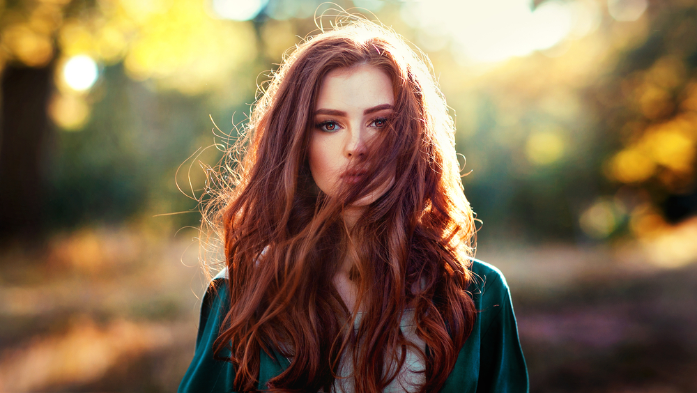 Người phụ nữ có mái tóc đỏ, một trong những màu tóc đẹp nhất cho đôi mắt xanh, đang đứng gợi cảm trong một khu rừng