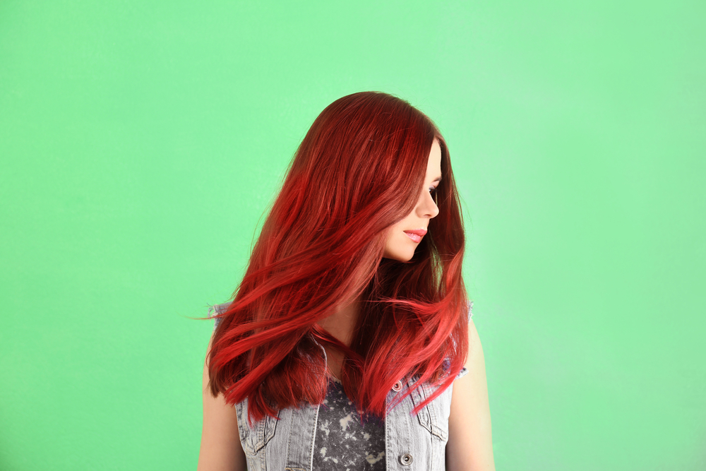 Juicy Cherry ginger hair color idea on a woman in a jean jacket in a green room