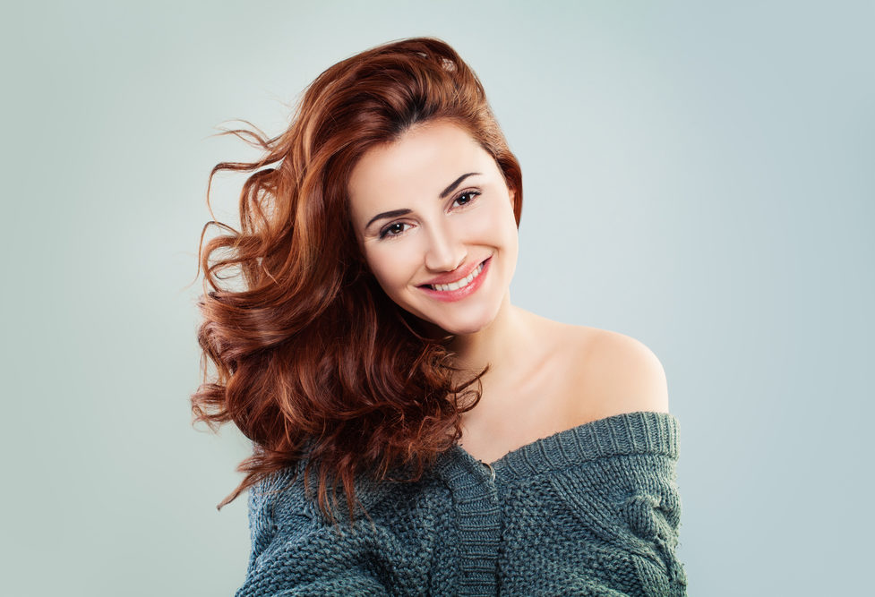 For a piece on the best winter hair colors, a woman with Deep Auburn hair in a sweater smiles