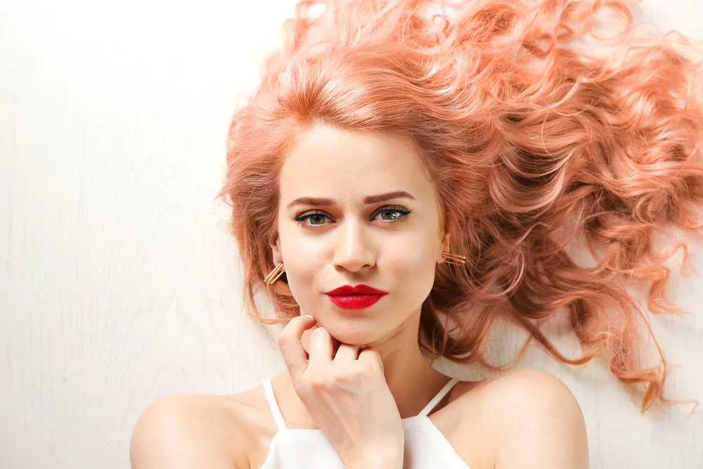 Warm Copper-Washed Coral Rose Gold Hair Color on a woman lying down