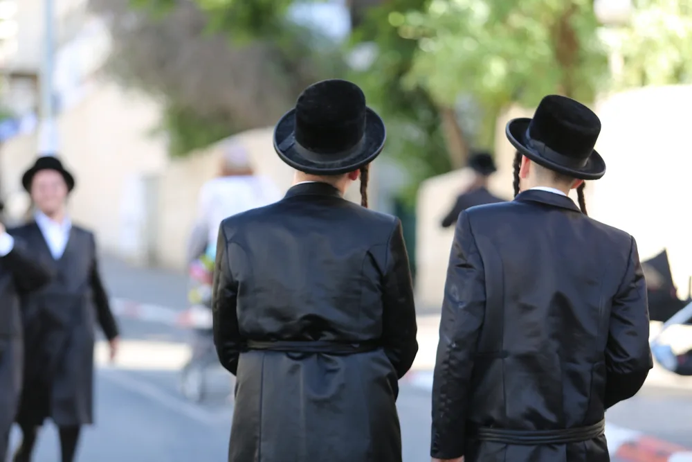 Two Jewish men with payots walking along a street and talking while wearing hats