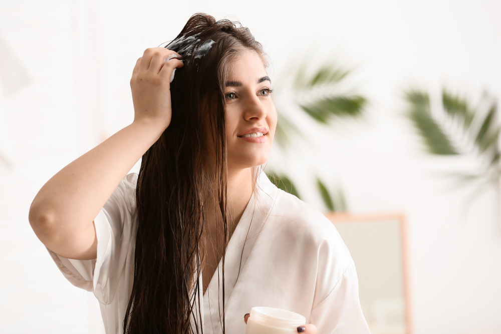 Woman applying conditioner to her hair in a bath robe