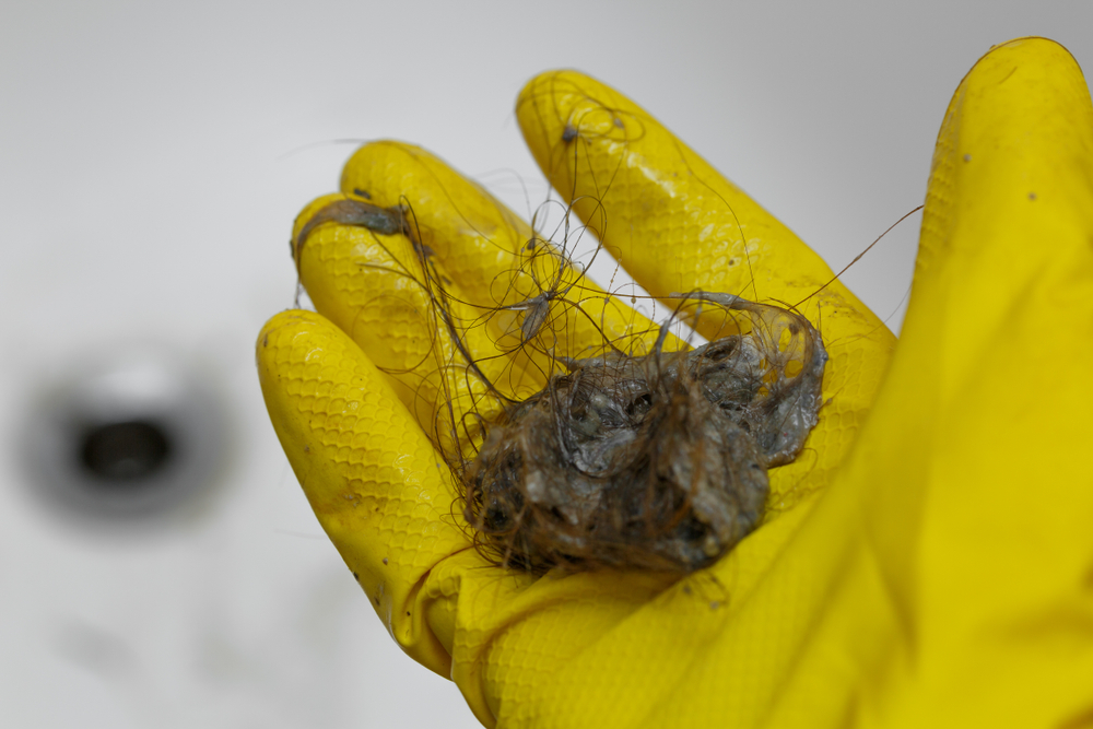 Close up of a man holding a clump of hair in his yellow glove