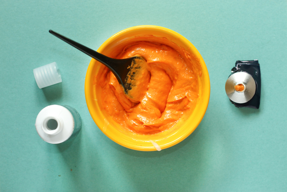 Layflat image with orange dye in a yellow bowl for a piece on does permanent hair dye fade