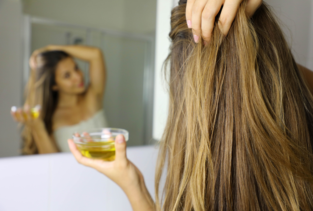 Woman looking in the mirror removing permanent hair dye with olive oil