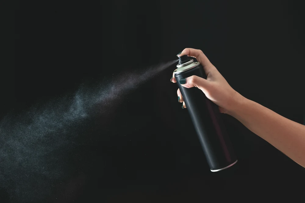 Someone spraying a can of hair spray in a black room