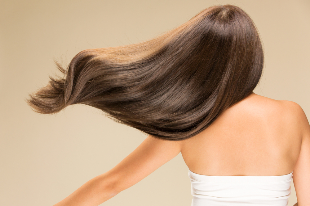 Woman letting her shiny hair blow in the wind on a brown background for a piece titled are silicones bad for your hair
