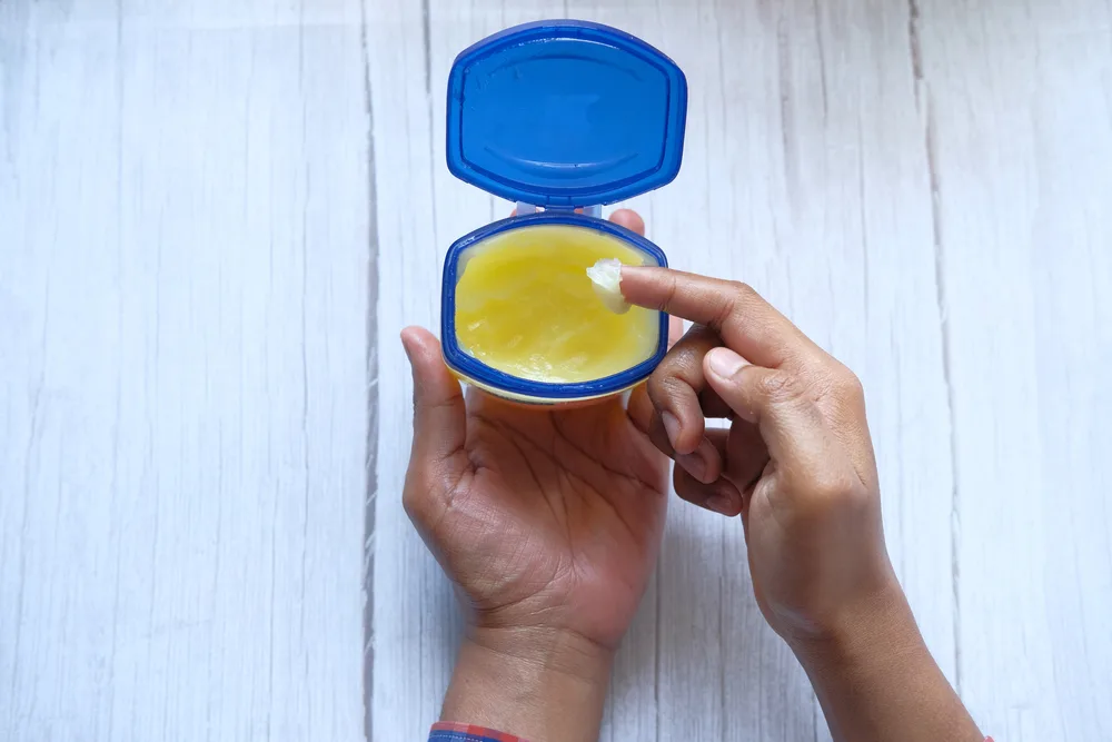 Man putting his hand in a container of petroleum jelly for a piece on how to get hair dye off scalp but not hair