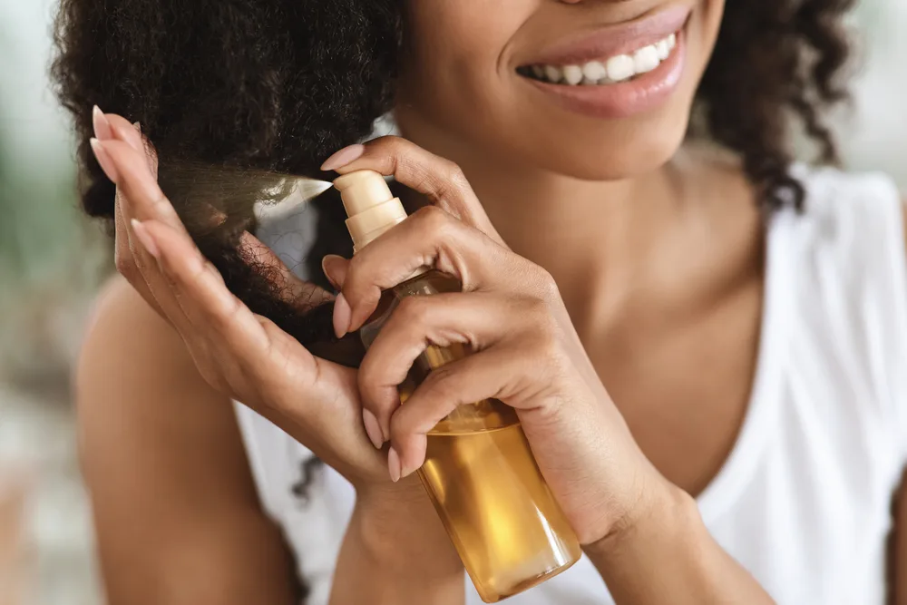 Woman spraying oil in her hair for a piece on the best relaxer alternatives for black hair