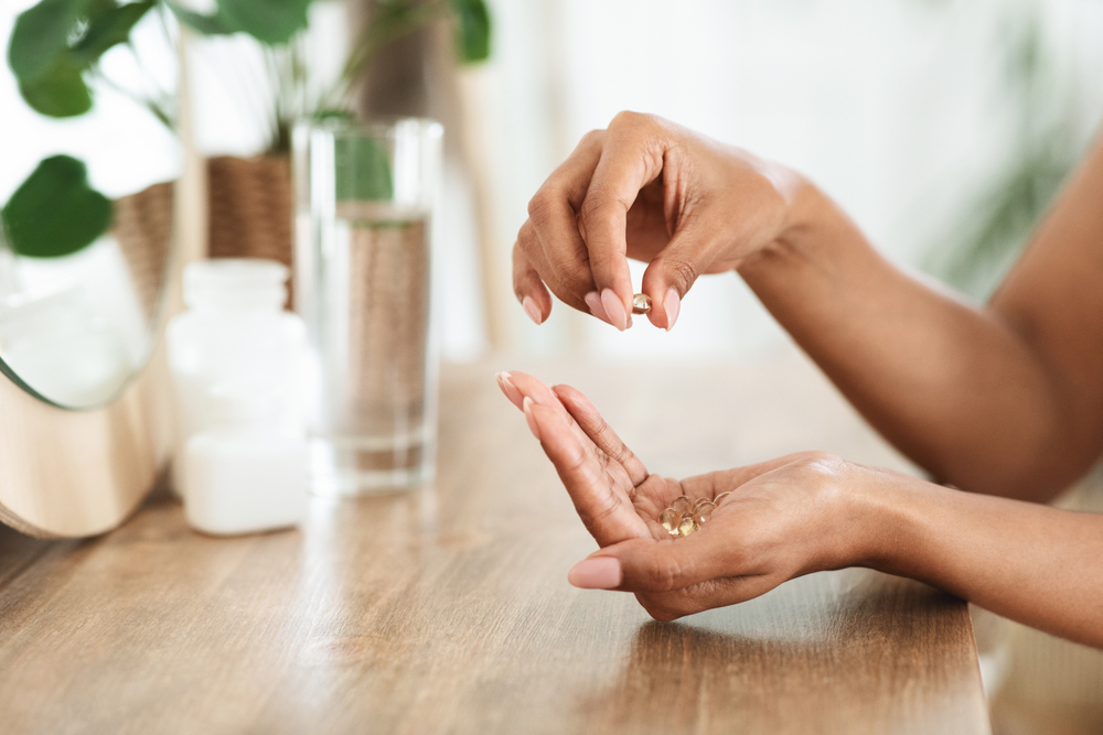 Woman taking biotin putting the pills into her cupped hand next to a glass of water