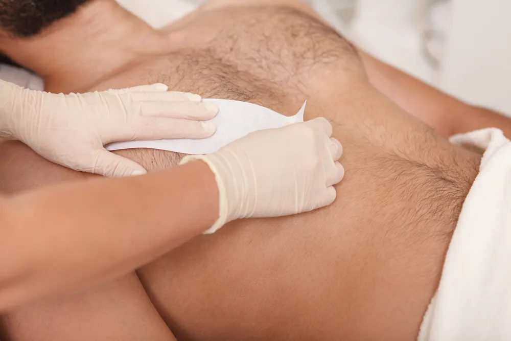 To help explain what manscaping is, a woman in gloves waxing a man's hairy chest