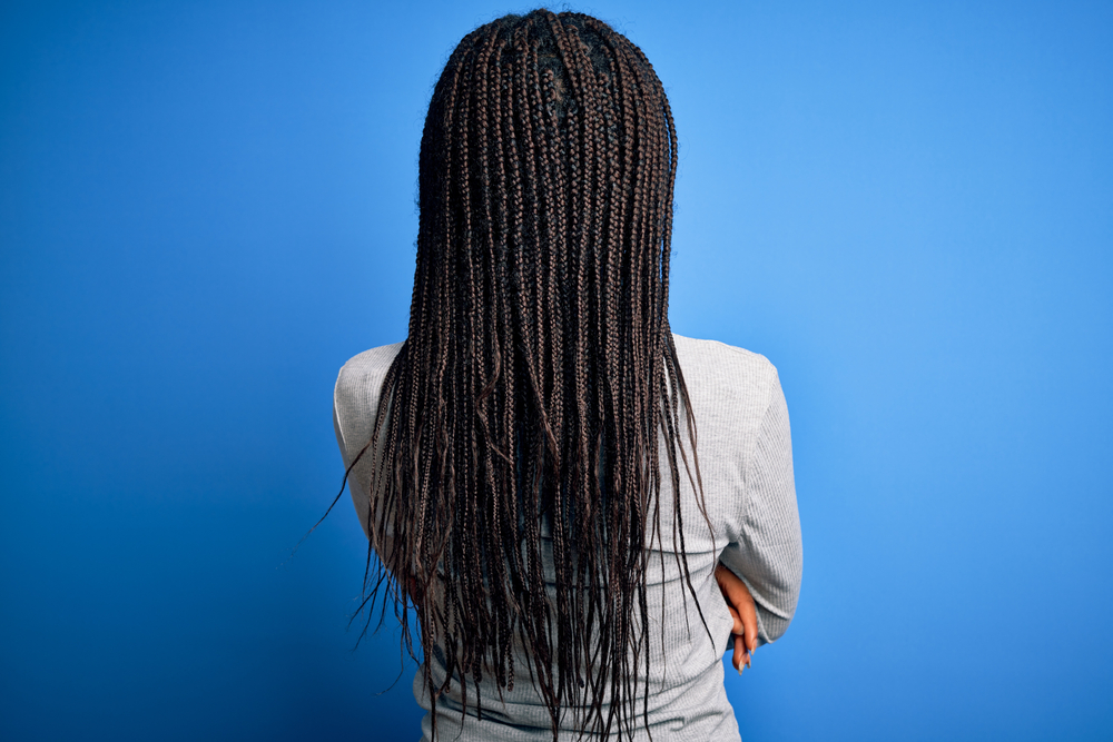 Người phụ nữ với bím tóc hộp trong căn phòng màu xanh lam để xem một đoạn về cách sửa những bím tóc xoăn rối