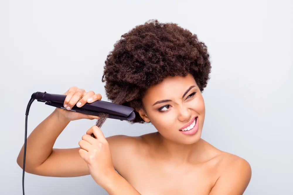 Image of a black woman straightening her hair with heat for a piece on relaxer alternatives for black hair