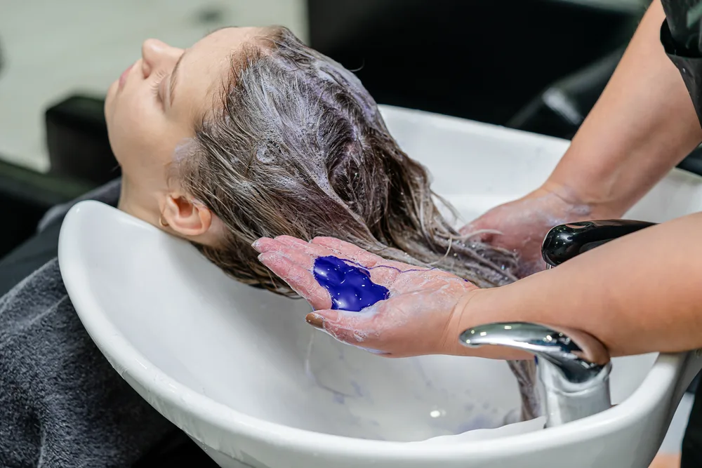 Woman using purple shampoo in a salon chair to make her hair color last longer