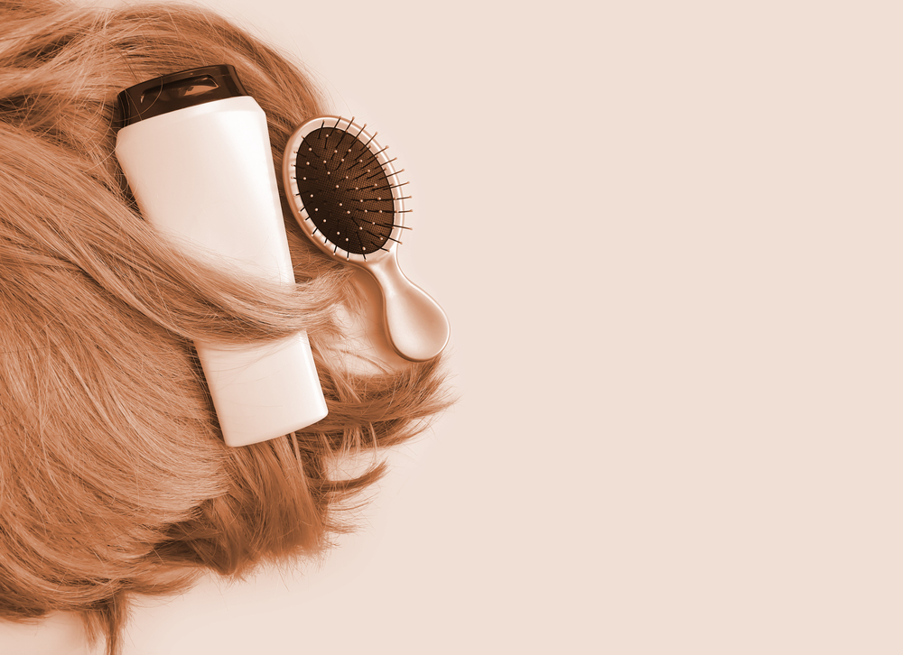 Image for a guide showing us how to wash a weave with hair products and a brush on brown hair on a light pink background