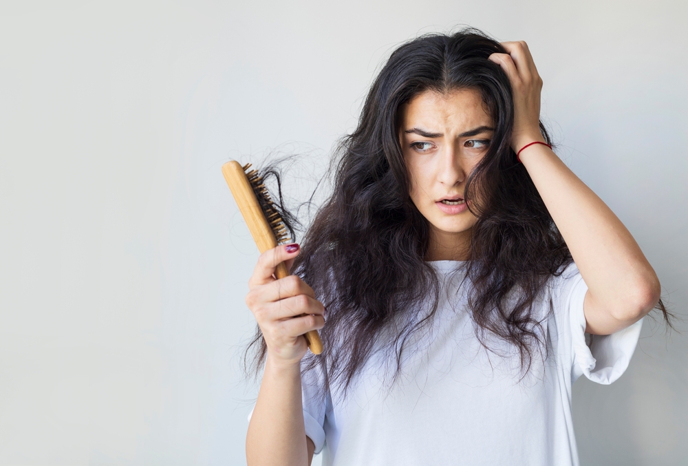For a guide titled can you leave conditioner in your hair, a woman looking at a brush with hair breakage