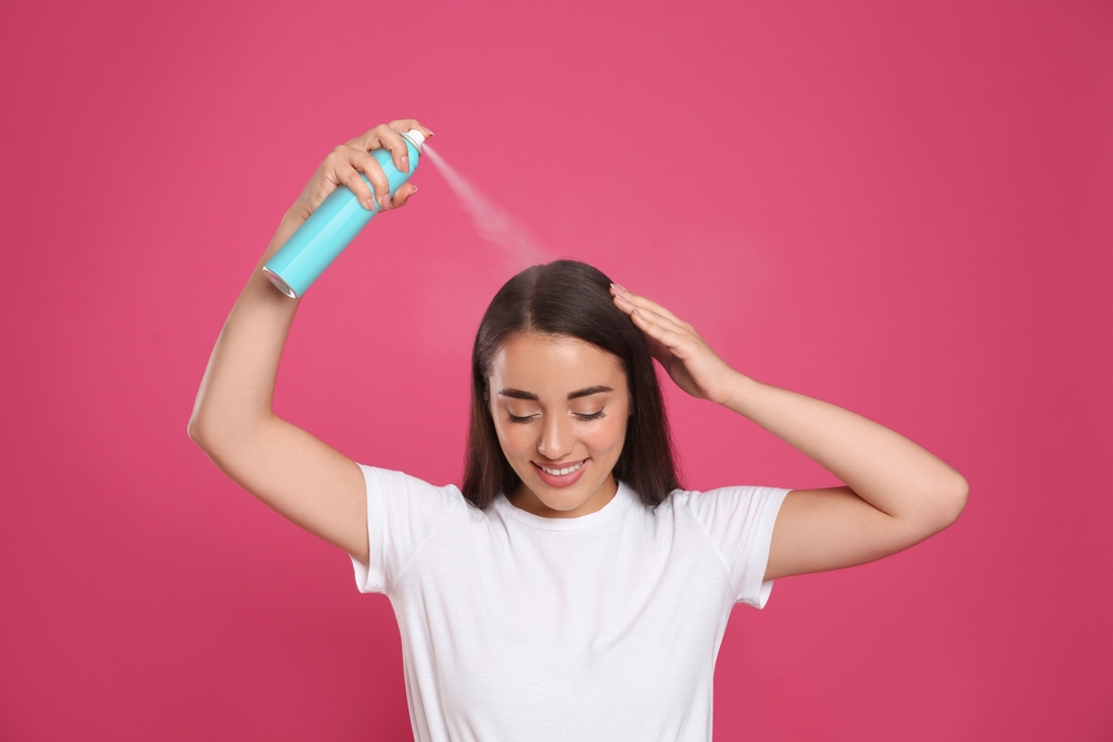 Woman using dry shampoo as a hairspray alternative in a pink room