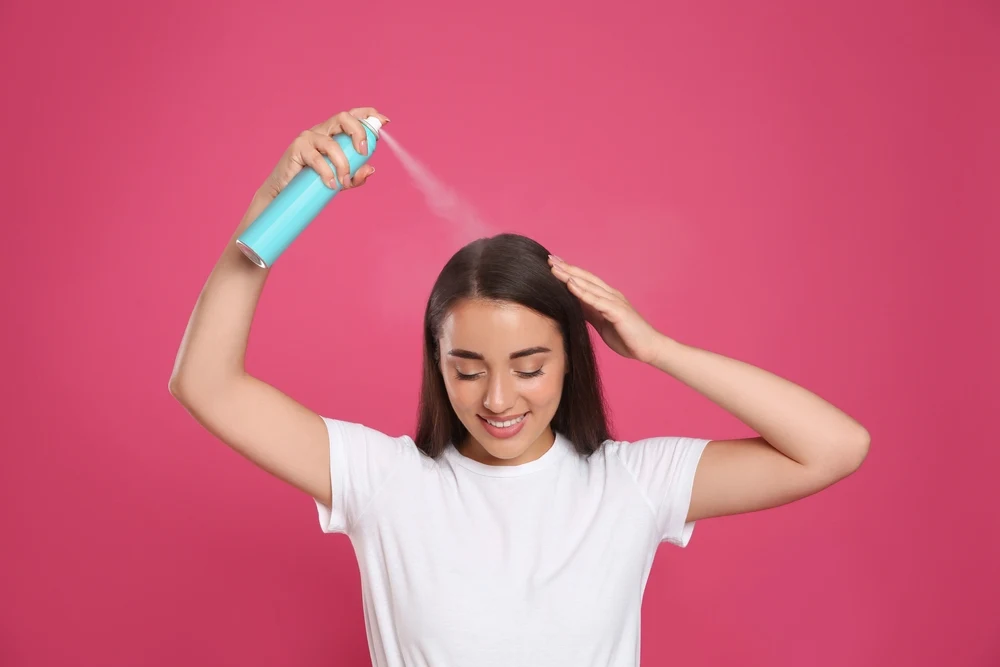 Woman using dry shampoo as a hairspray alternative in a pink room