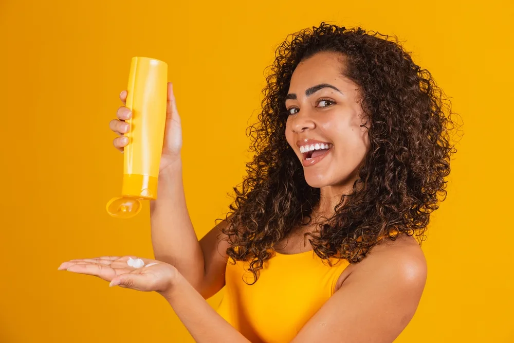 Woman with hair cream pictured squirting it in her hand for a piece on the best relaxer alternatives for black hair