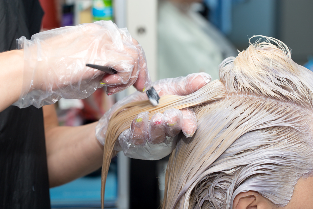 Woman in a salon getting her hair bleached by a hairdresser in rubber gloves