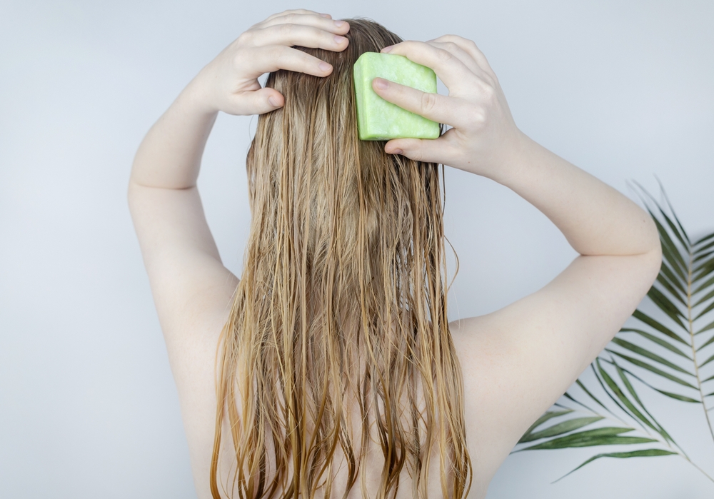 Người phụ nữ chăm sóc mái tóc đã tẩy trắng của mình đang rụng bằng cách sử dụng một thanh dầu gội đầu