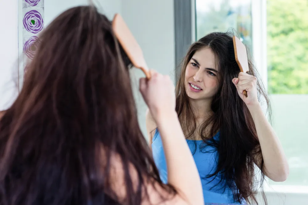 Image for a guide to how to straighten frizzy hair featuring a woman pulling a wooden brush through her hair