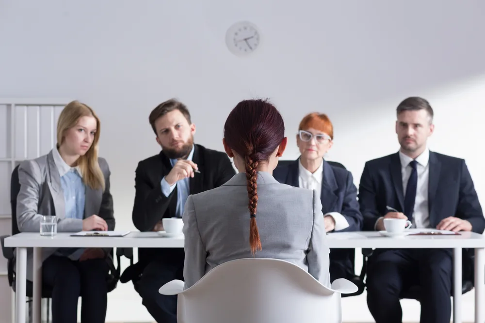 Lady in a job interview with a braided ponytail looks at four people in front of her