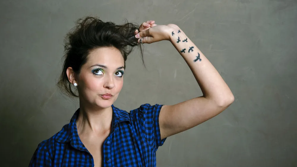 Woman playing with her hair because she's anxious with bird tattoos on her forearm