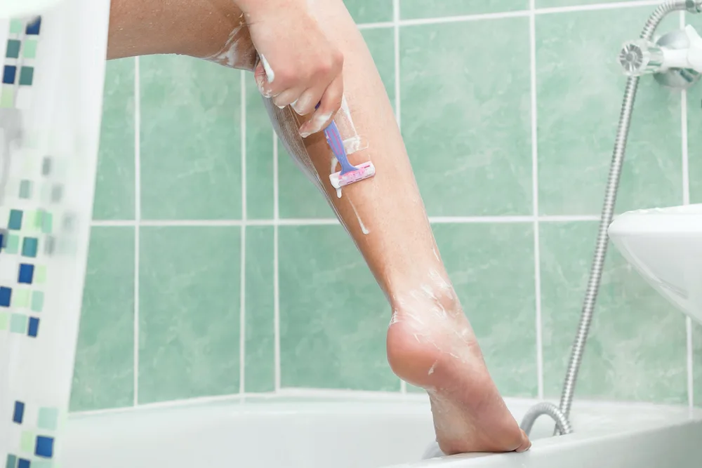 Woman in a shower shaving her legs for a piece on why does leg hair grow so fast