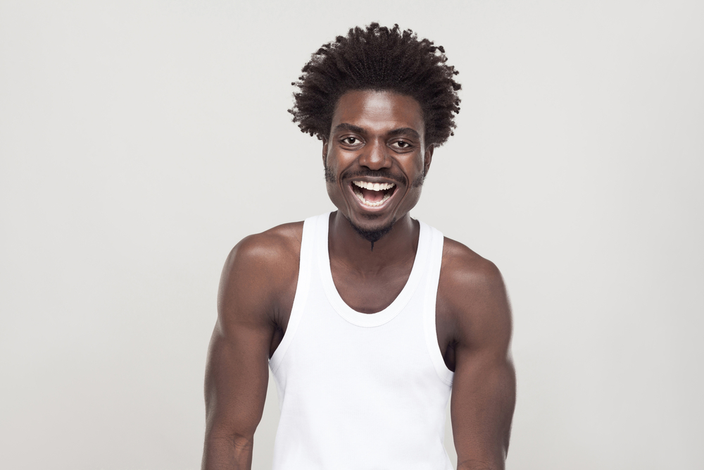 For a roundup of black men with perms, a guy in a white shirt smiles in a grey room