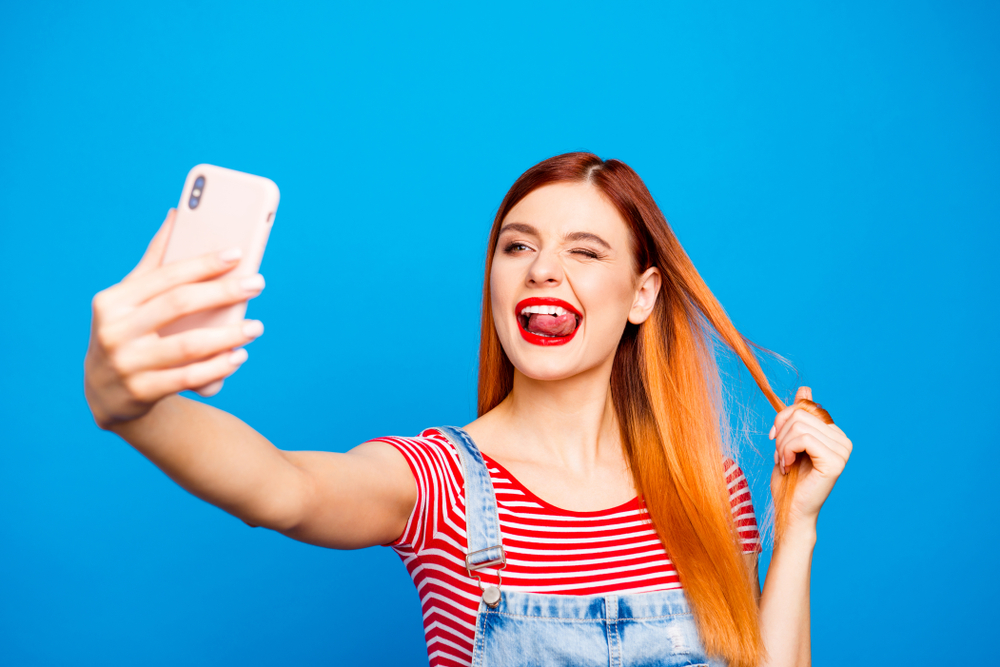 Woman taking a selfie in jean overalls for a piece on red hair captions for instagram