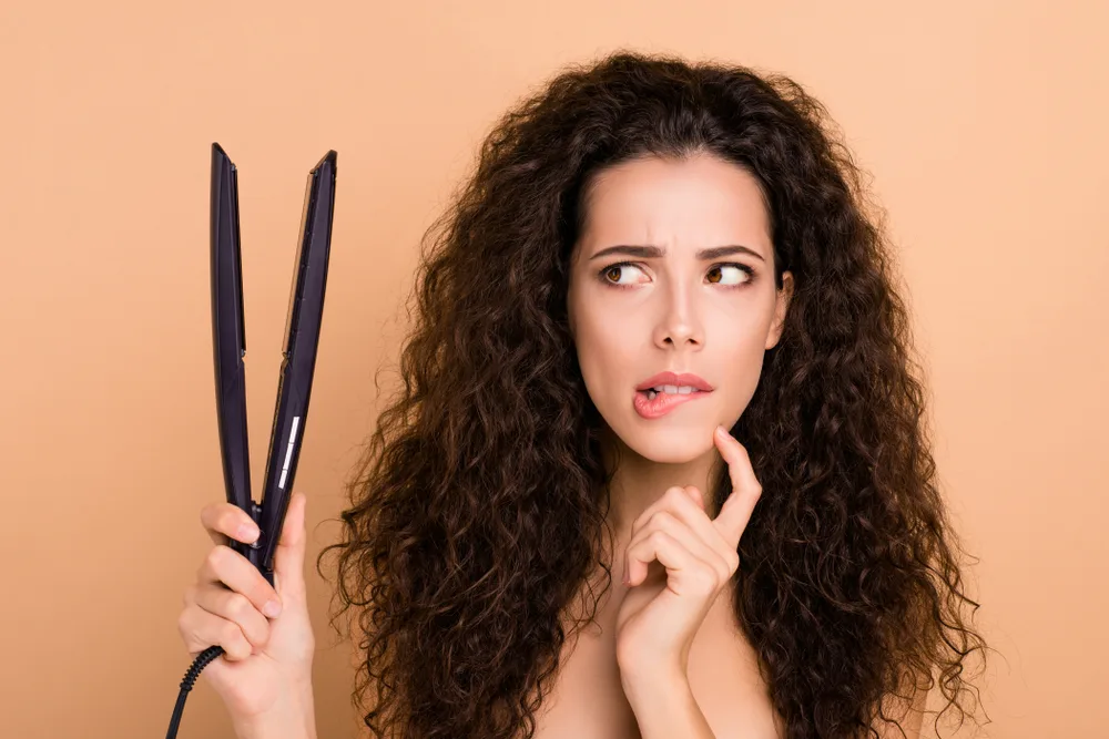 Image of a woman holding up a flat iron and wondering, 