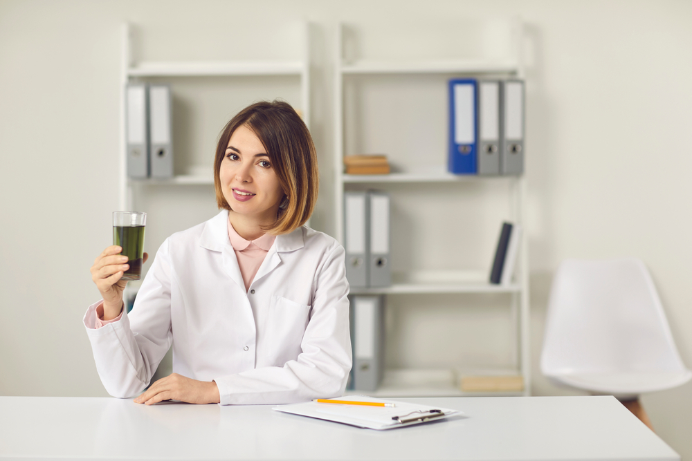 Nutritionist at a desk holding a smoothie in a glass up to highlights the benefits of chlorophyll on hair