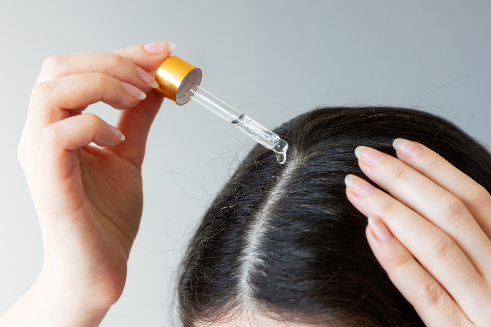 Woman putting oil on her head and wondering when she'll see the signs of new hair growth