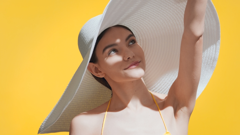 Woman wearing a hat and smiling and wondering what is scalp sunscreen