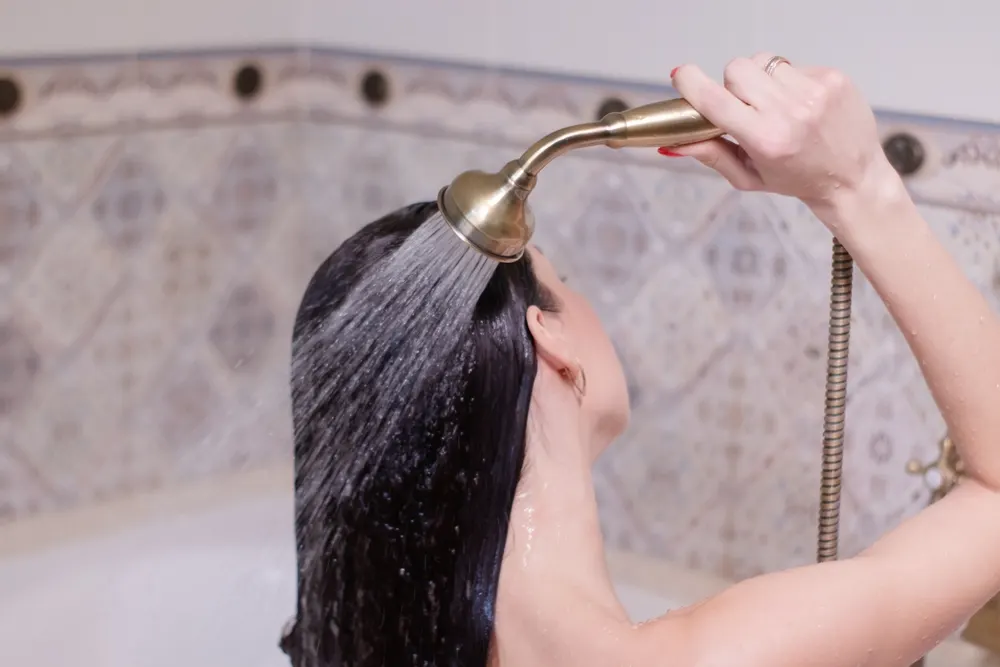 Woman using the water only method to wash her hair by rinsing it with a shower nozzle