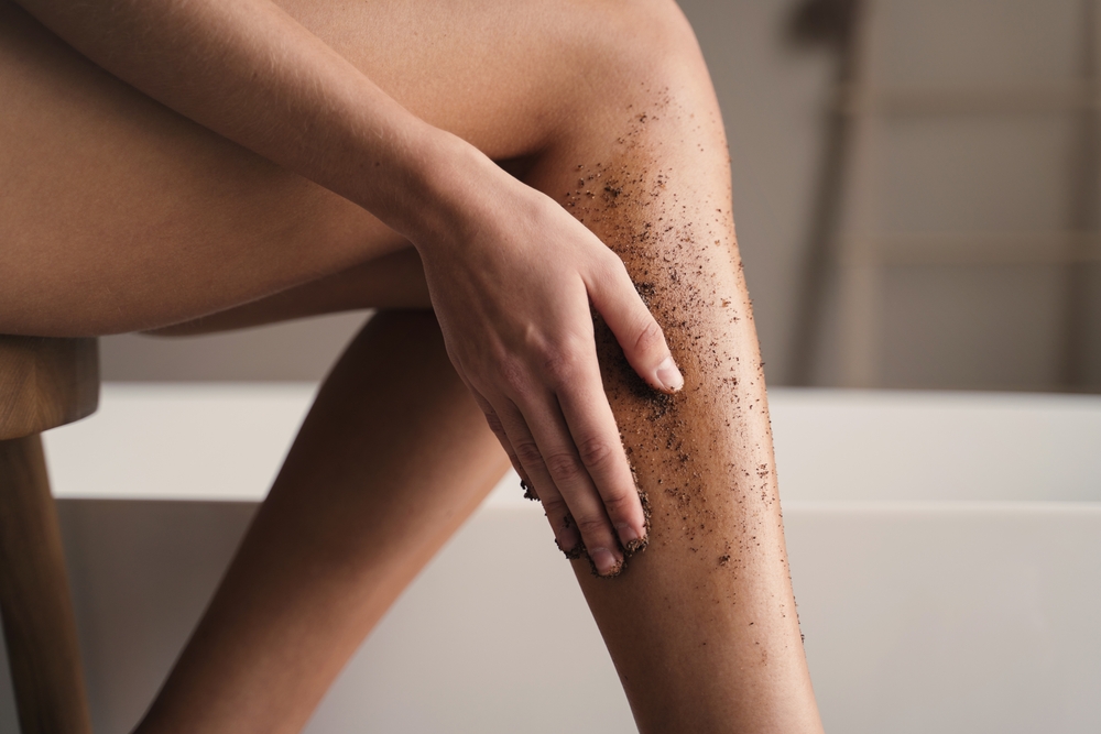 Woman exfoliating her legs for a piece titled should i exfoliate before or after shaving