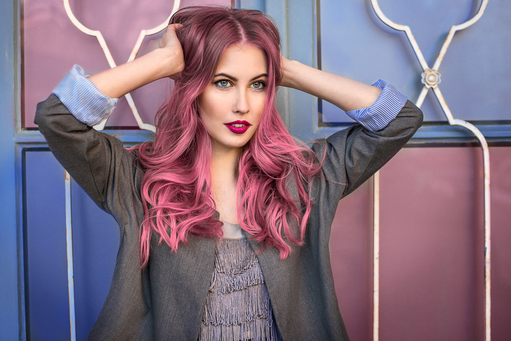 Woman rocking an unnatural hair color for pale skin in a jean jacket outside a pink and purple wall