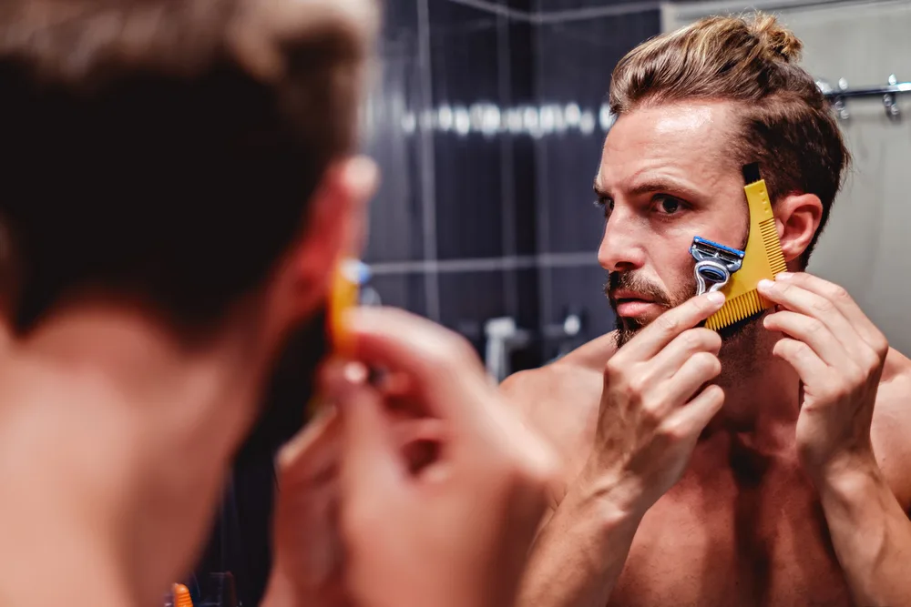 Man shaping his beard with a shaper tool while looking in the mirror